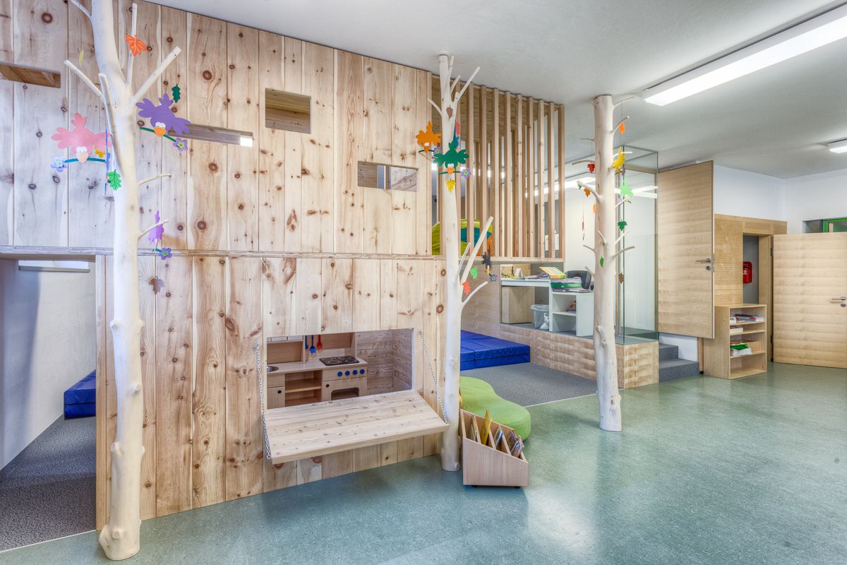 Ein farbenfrohes Spielzimmer mit Holzwänden, Baumelementen und einer kleinen Küche, das die Kreativität und Entdeckungsfreude der Kinder fördert.